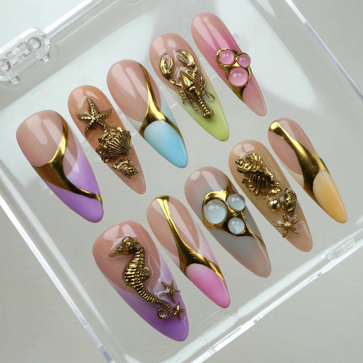 Press-on nails by Donailsart with gold under-the-sea elements on pastel ombré designs