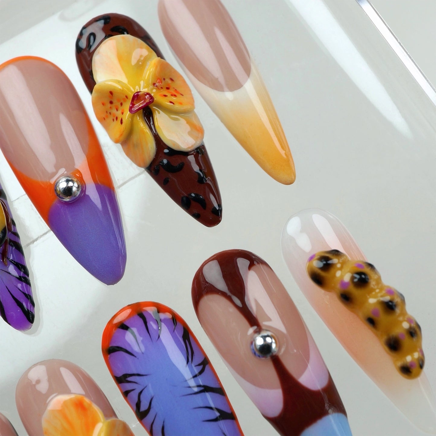 High-fashion press-on nails by Donailsart with modern shapes, chrome studs, and tropical jungle-inspired motifs