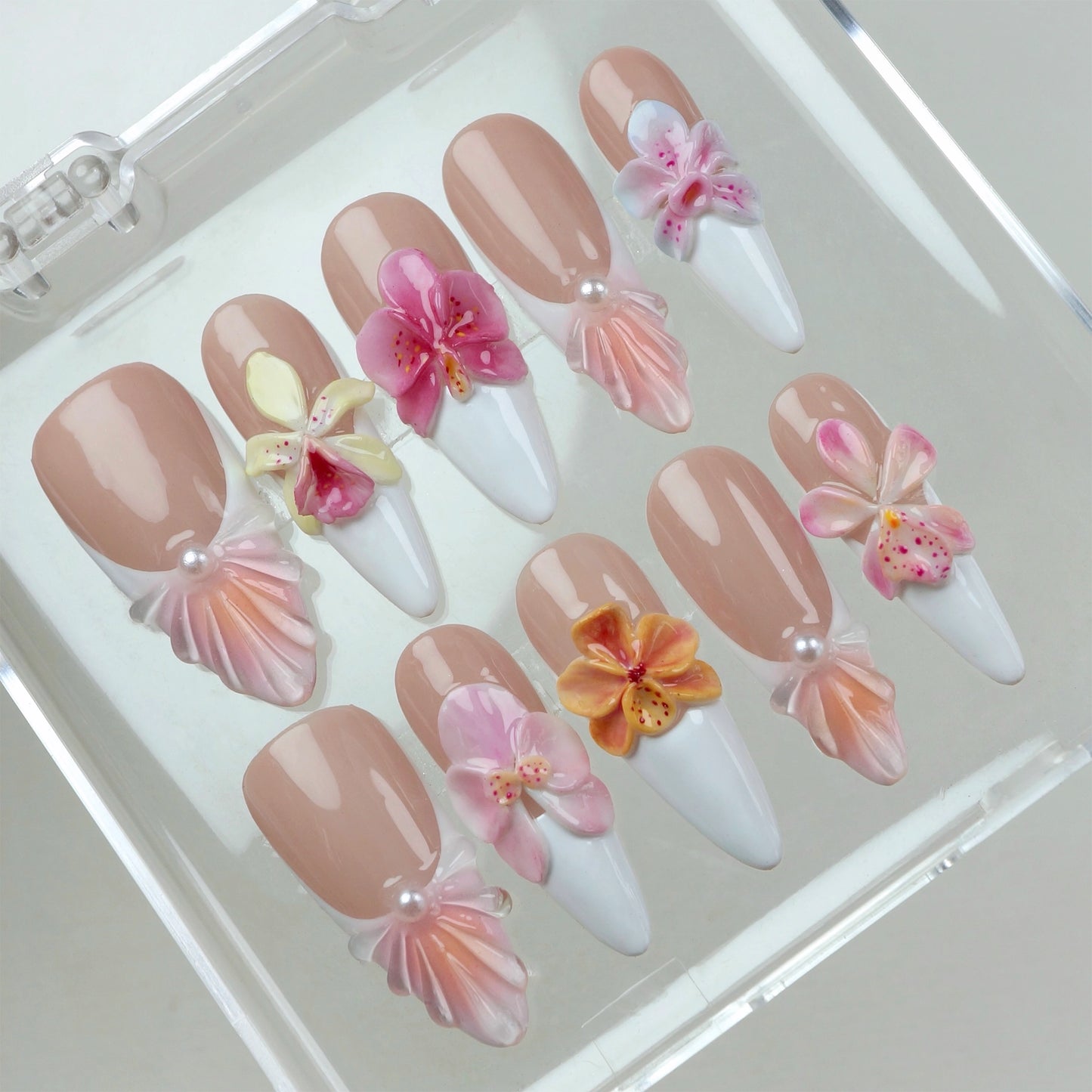 Set of flower nails featuring nude and white French tips, 3D orchids in pink, yellow, and orange, and pearl embellishments