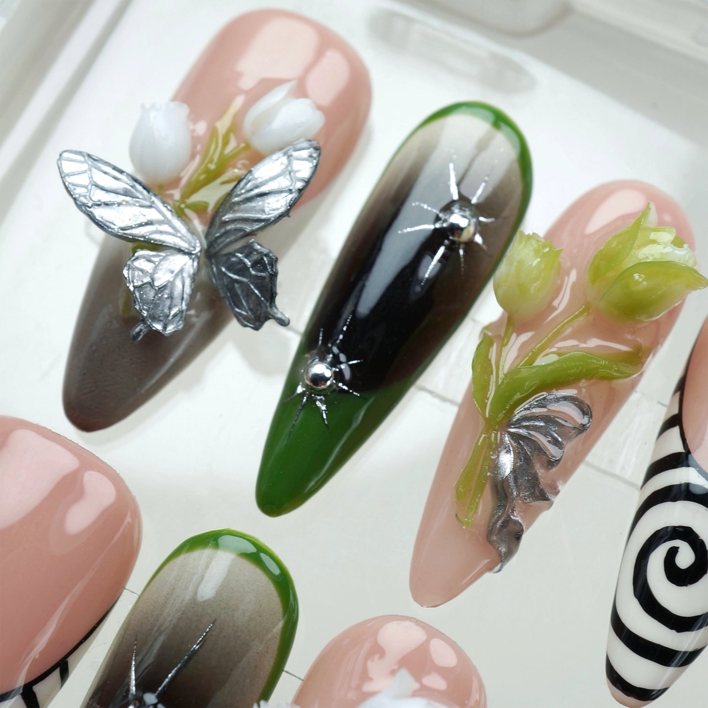 Bold flower nails with surreal spiral art, black and green gradients, and silver 3D floral motifs on a nude base