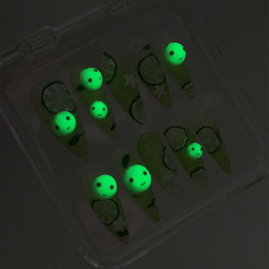 Smiski-inspired press-on nails by Donailsart with lime green tones, citrus slice details, and glowing mini smiski faces for a fun, quirky vibe