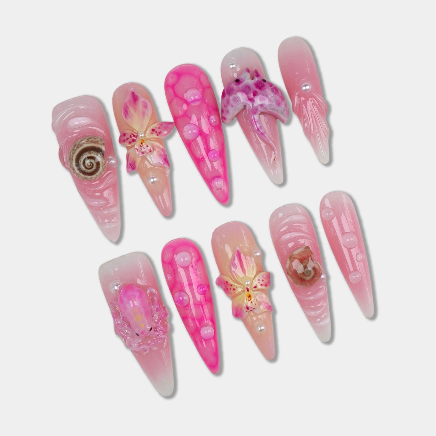 Delicate summer nails in pink tones with 3D seashells, florals, and water droplet accents for a beachy feminine vibe.