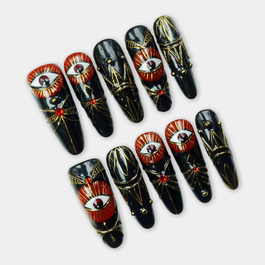 Striking black press-on nails with red evil eye designs, gold details, and gemstone accents – a powerful statement set by Donailsart