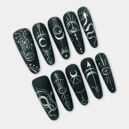 Black press-on nails with white mystical symbols including moons, eyes, snakes, and arrows – a bold and spiritual design by Donailsart