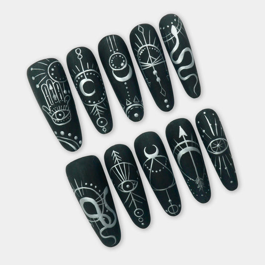 Black press-on nails with white mystical symbols including moons, eyes, snakes, and arrows – a bold and spiritual design by Donailsart