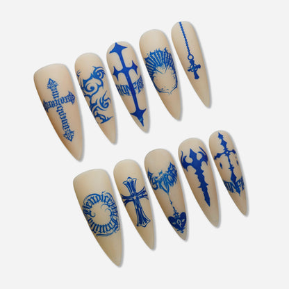 Blue Heresy press-on nail set by Donailsart – muted nude nails with sharp cobalt blue cross symbols, distorted typography, and tattoo-inspired graphic markings