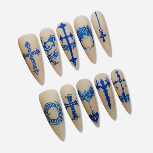 Blue Heresy press-on nail set by Donailsart – muted nude nails with sharp cobalt blue cross symbols, distorted typography, and tattoo-inspired graphic markings