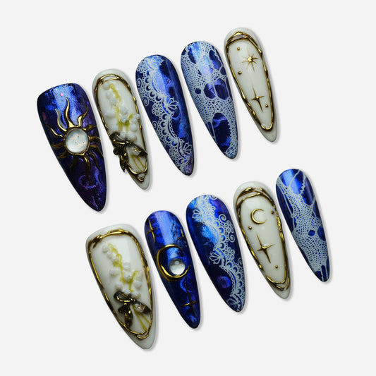 Celestine Sovereign press-on nail set by Donailsart – metallic cobalt chrome nails with white lace overlays, gold celestial moon and star frames, and opal centerpiece accents