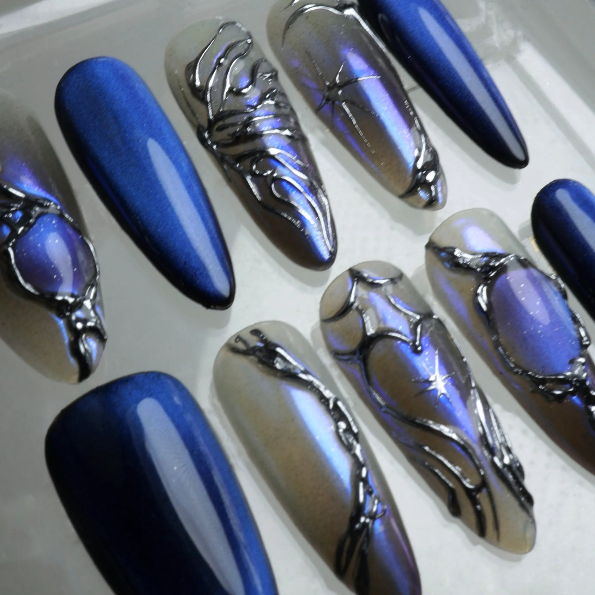 Dark press-on nails with glowing blue magnetic polish and silver frame embellishments