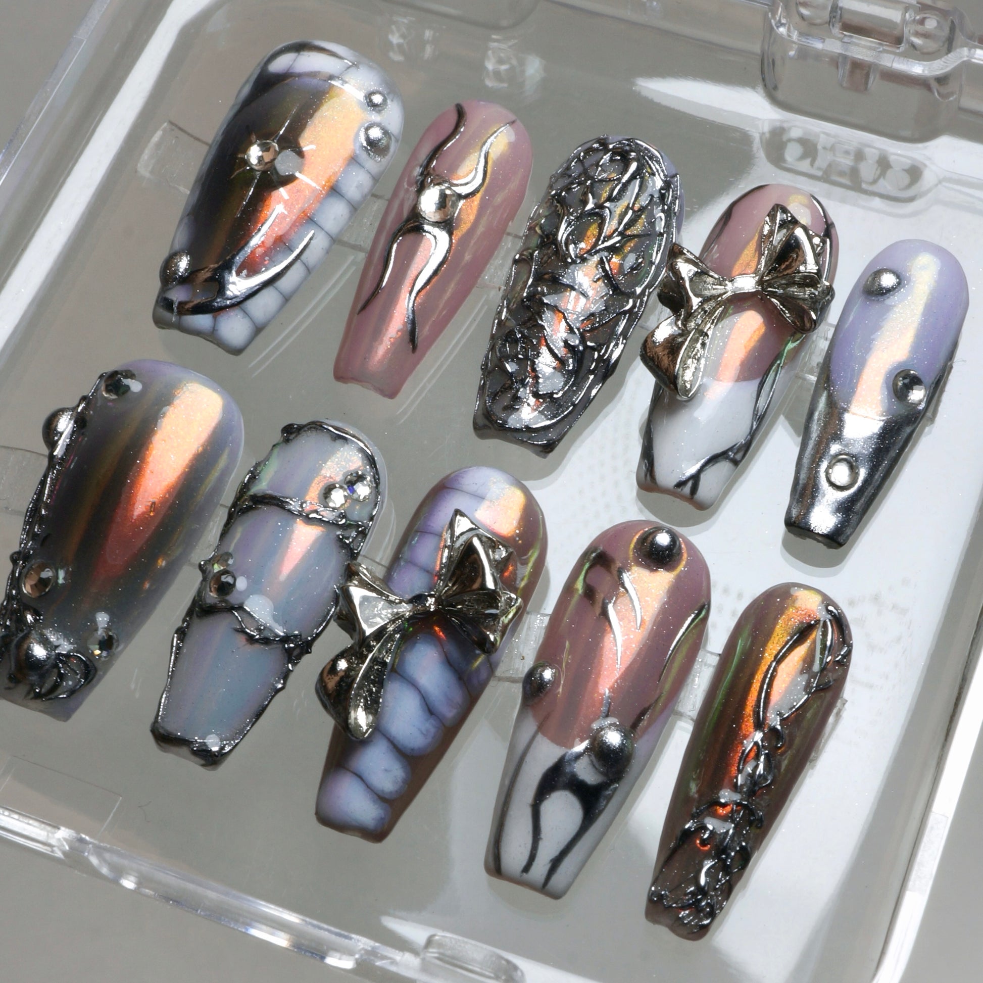 Edgy press-on nails featuring reflective rose chrome, sculpted silver charms, and barbed-wire inspired textures.