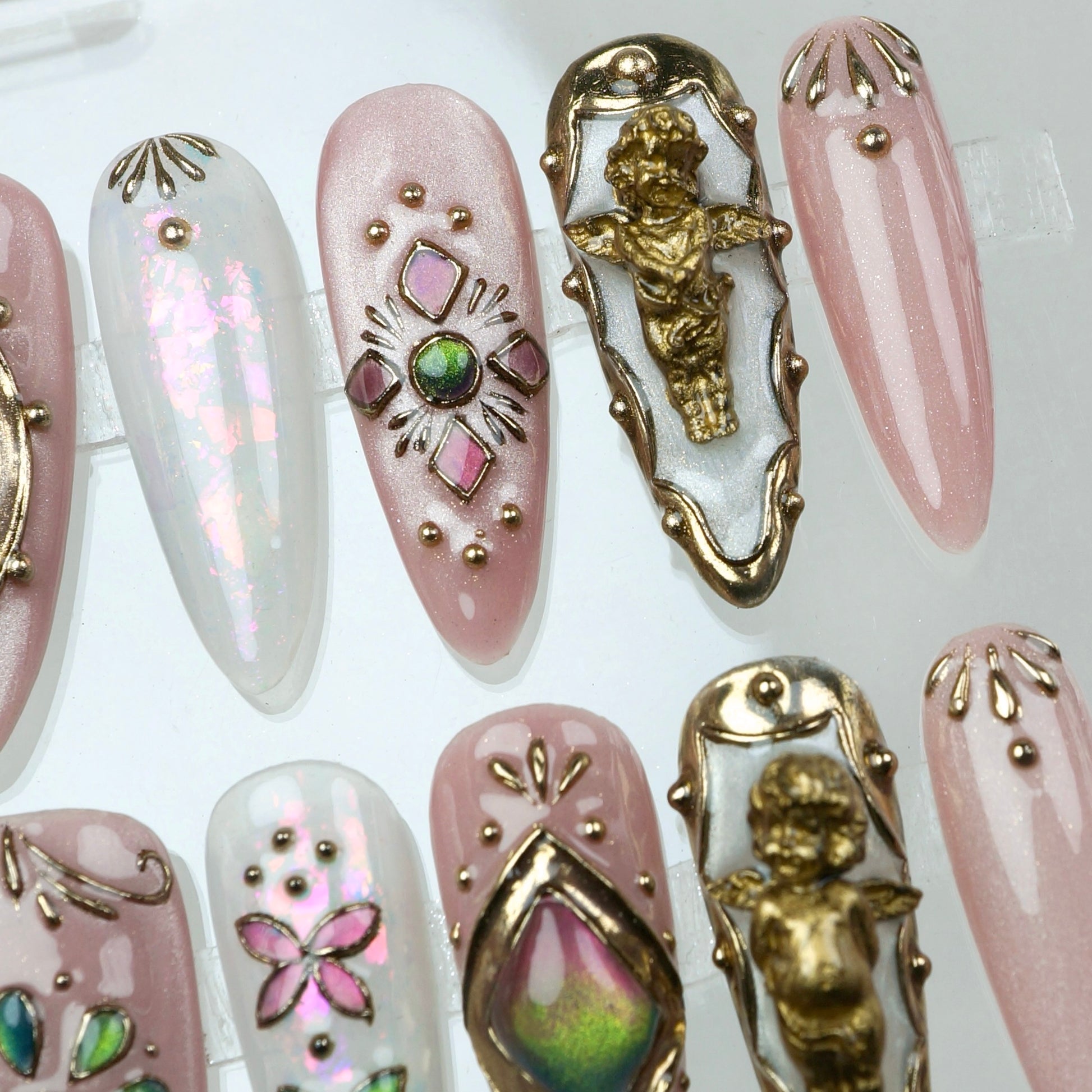 Blush pink press-on nails adorned with golden cherubs, sparkling stones, and delicate florals – like a fairytale on your fingertips.