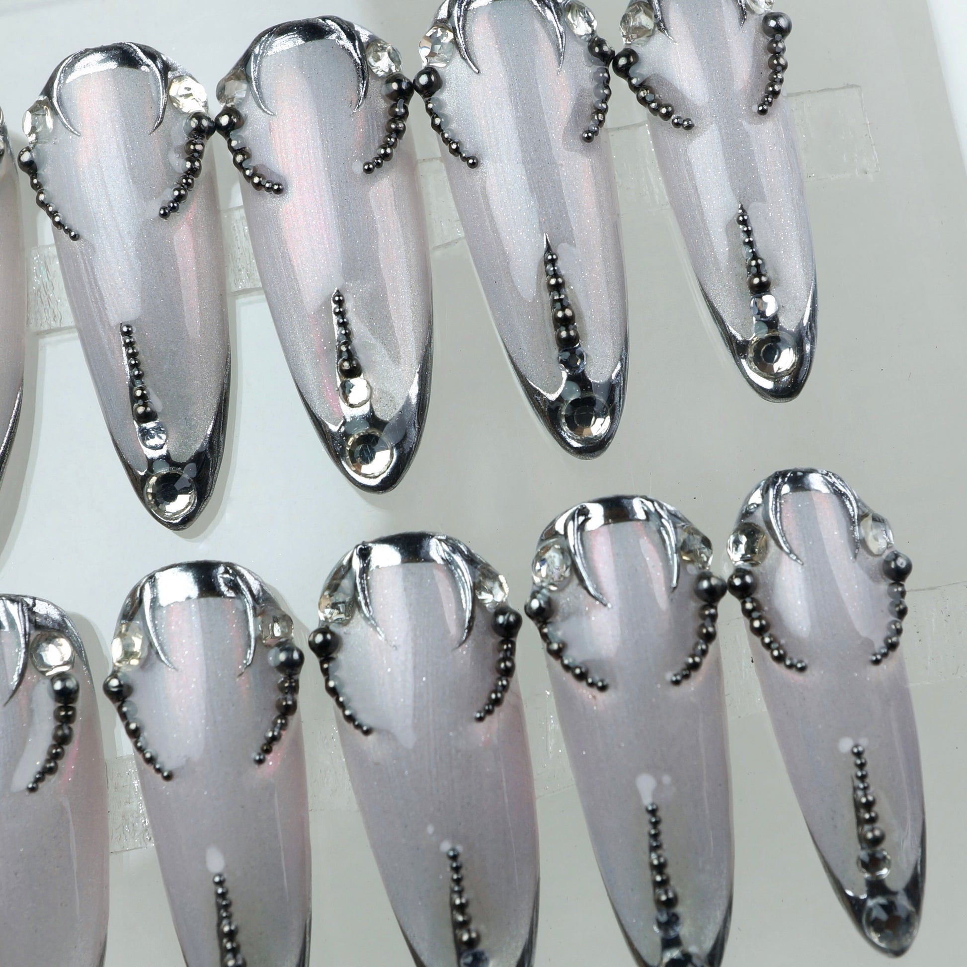 Sharp and sleek, these metallic press-on nails feature dark chrome edges and beadwork like a digital lace tattoo.