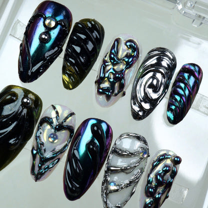 Iridescent press-on nails with sculpted black chrome designs and silver 3D detailing – a bold, high-fashion nail art look.