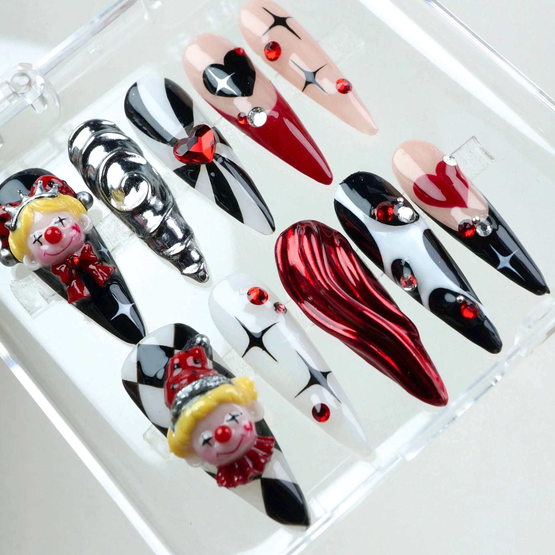 Clown nails with harlequin-style patterns, glossy red chrome swirls, and detailed clown charms – design by Donailsart.