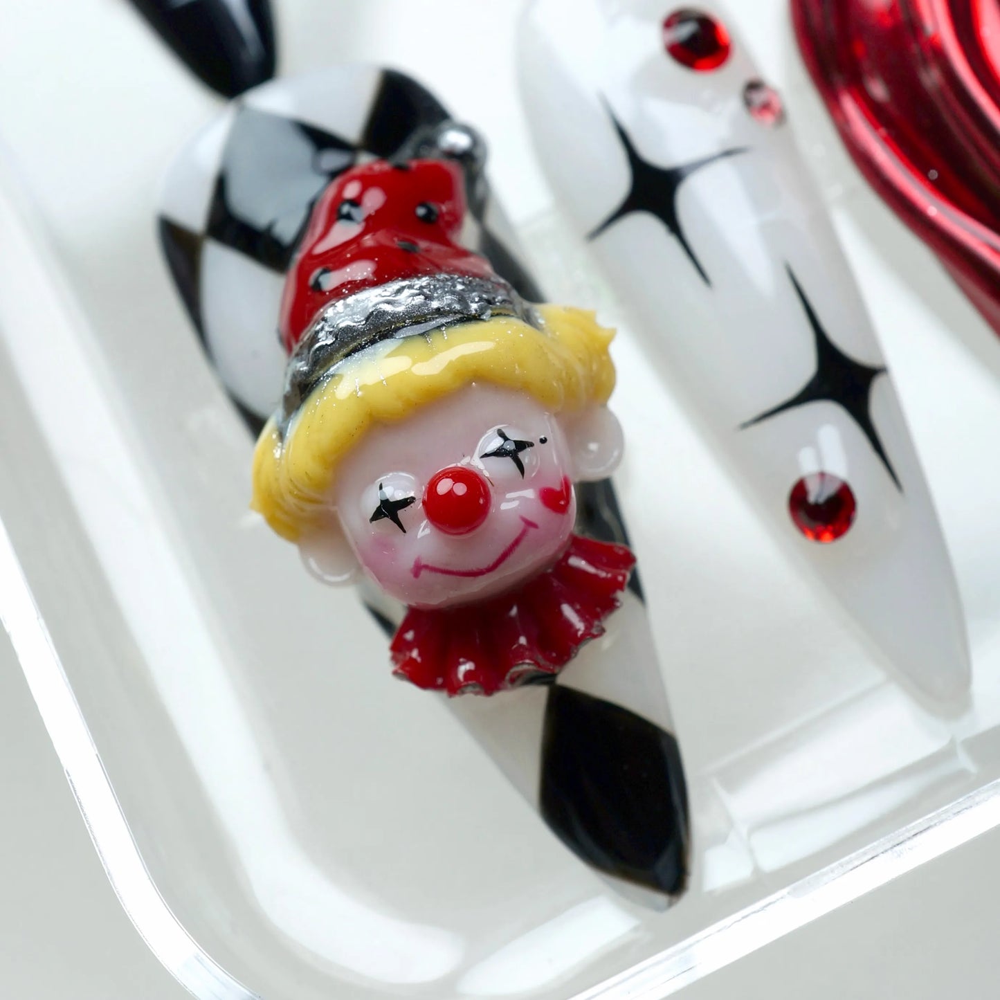 Bold clown nails by Donailsart, featuring 3D clown faces, diamond patterns, and heart accents in red, black, and white tones.