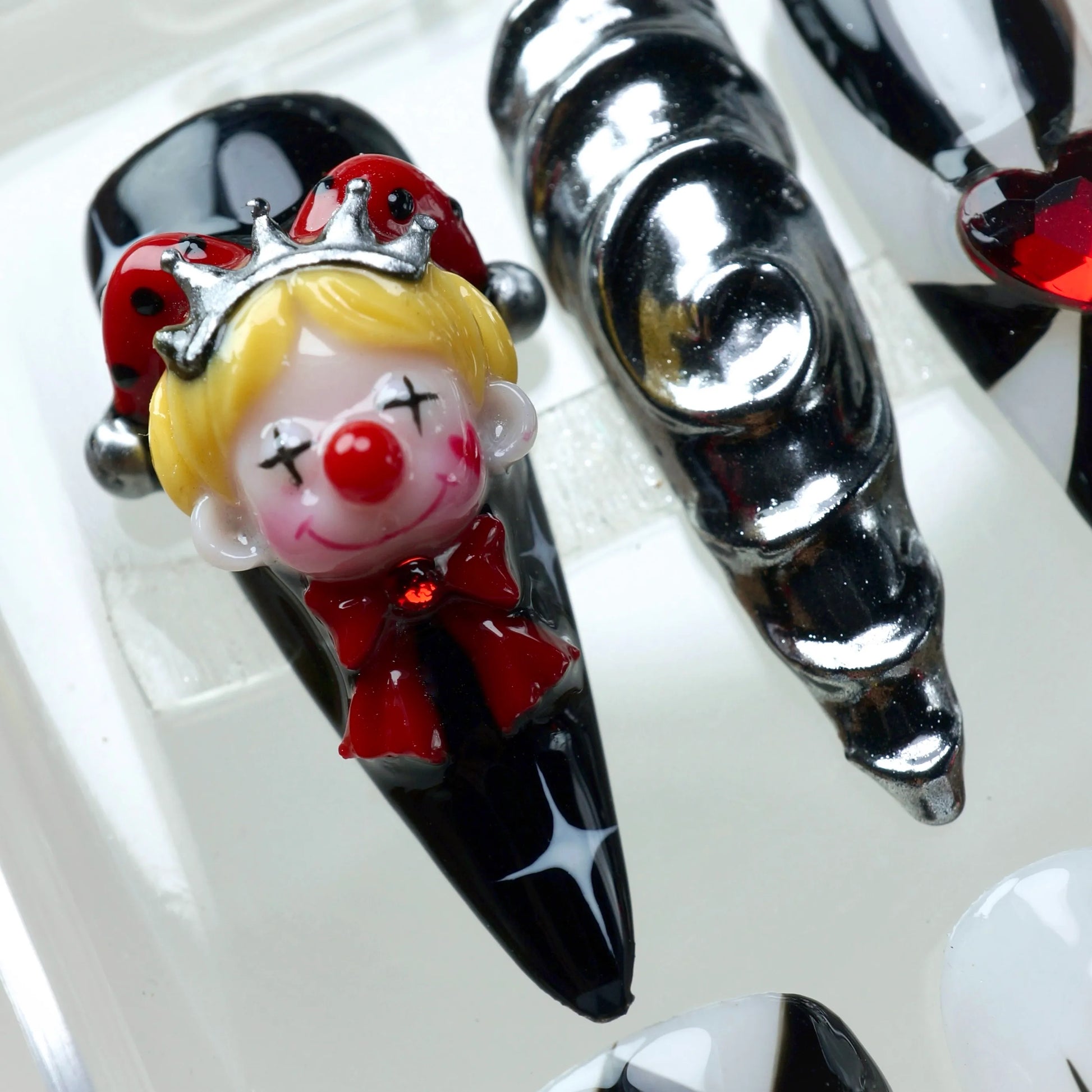 Clown nails with harlequin-style patterns, glossy red chrome swirls, and detailed clown charms – design by Donailsart.