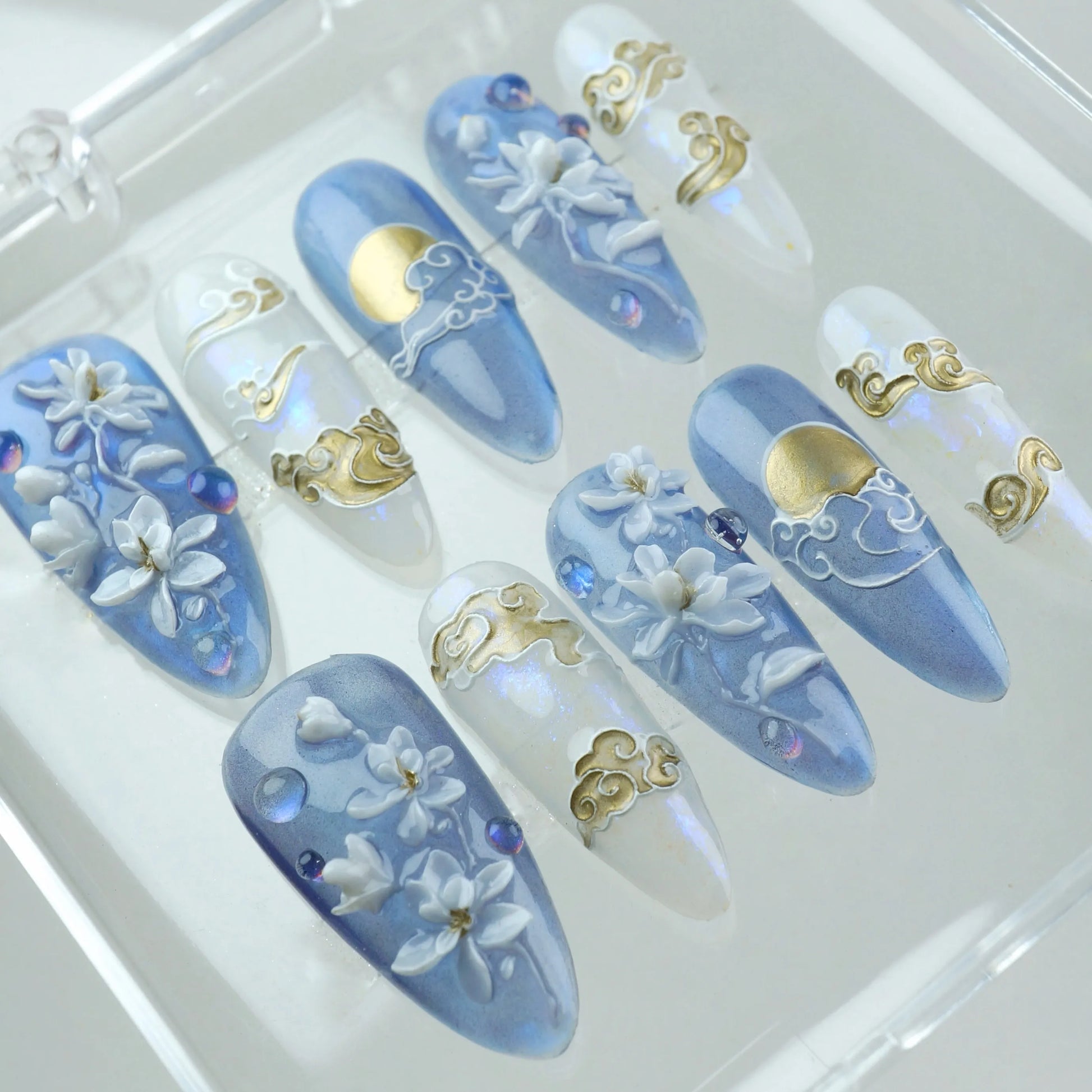 Dreamy press-on nails featuring moonlit skies, flowing gold clouds, and 3D white blossoms on a misty blue and opal base


