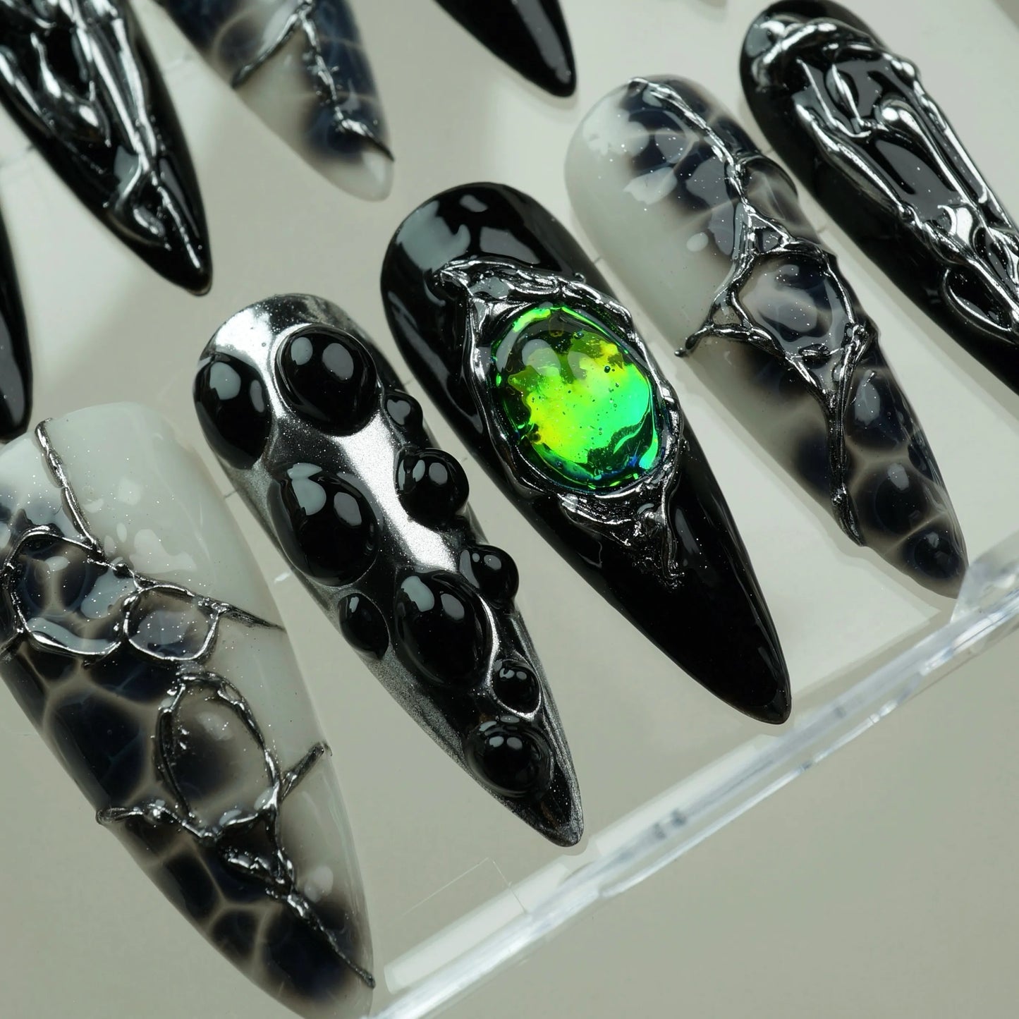 Emerald Enchantment press-on nails macro close-up in acrylic case – black bubble dot nails alongside iridescent green gem nail in chrome silver setting and smoky black-and-white marble textured nails