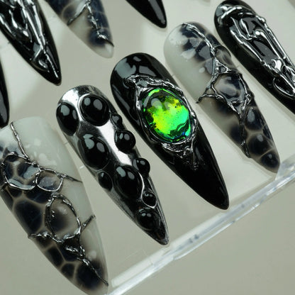 Emerald Enchantment press-on nails macro close-up in acrylic case – black bubble dot nails alongside iridescent green gem nail in chrome silver setting and smoky black-and-white marble textured nails