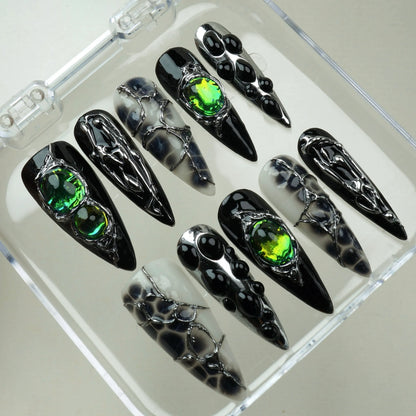 Emerald Enchantment press-on nails in open clear acrylic case – overhead angled view of full mixed design set with silver chrome drip art, iridescent green gemstones, and black-and-white marble ink nails