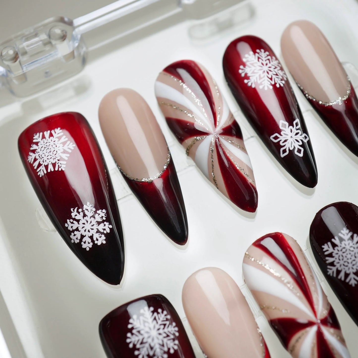 Holiday press-on nails with deep red shine, nude accents, and winter snowflake motifs from Donailsart
