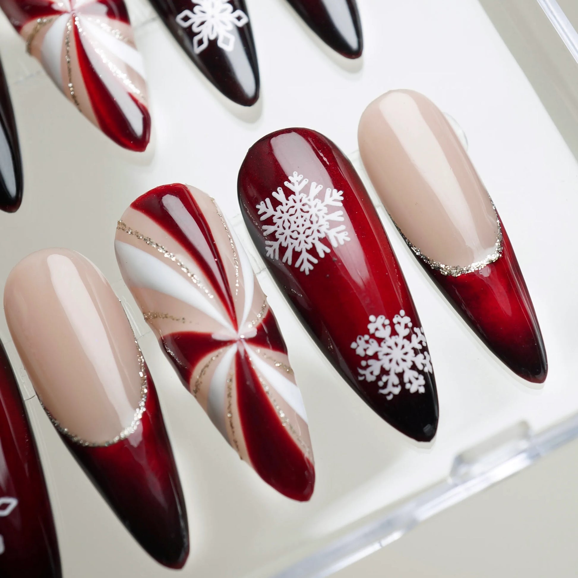 Almond-shaped holiday press-on nails with red ombré, nude tips, and festive snowflake art by Donailsart