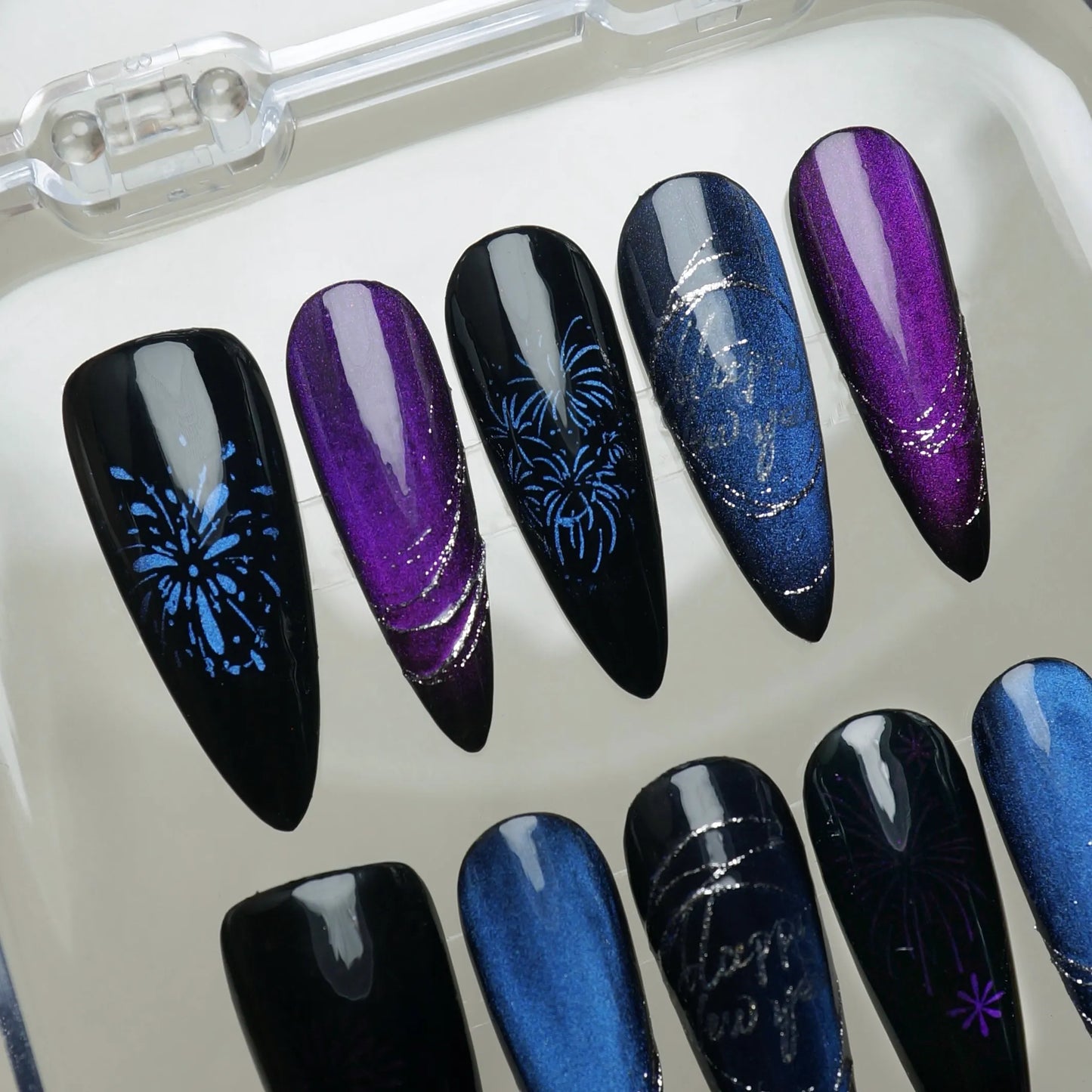 Black and midnight-blue cat-eye nails with silver swirl lines and purple firework patterns.