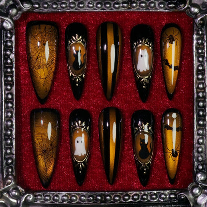 Amber Haunt press-on nails: amber-gold cat-eye nails with gold cameo frames of a ghost, black cat, bat and spider