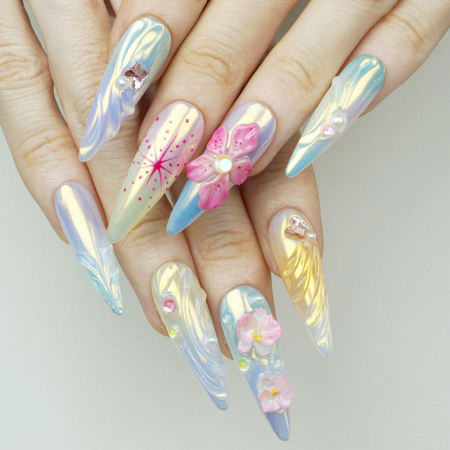 Flower Mirage press-on nails worn on hand model iridescent aurora stiletto nails with 3D pink flower charm hand-painted pink starburst firework art and holographic shimmer finish