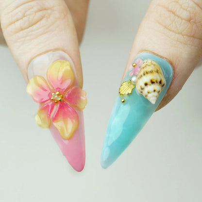Tropical Bliss press-on nail close-up showing large 3D hibiscus flower in yellow pink gradient and aqua nail with real 3D conch shell pink flower and gold scallop charm
