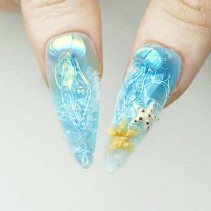 Ocean Bloom press-on nail close-up showing 3D iridescent jellyfish with flowing translucent tentacles and 3D white spotted starfish with orange flower charm on aqua base
