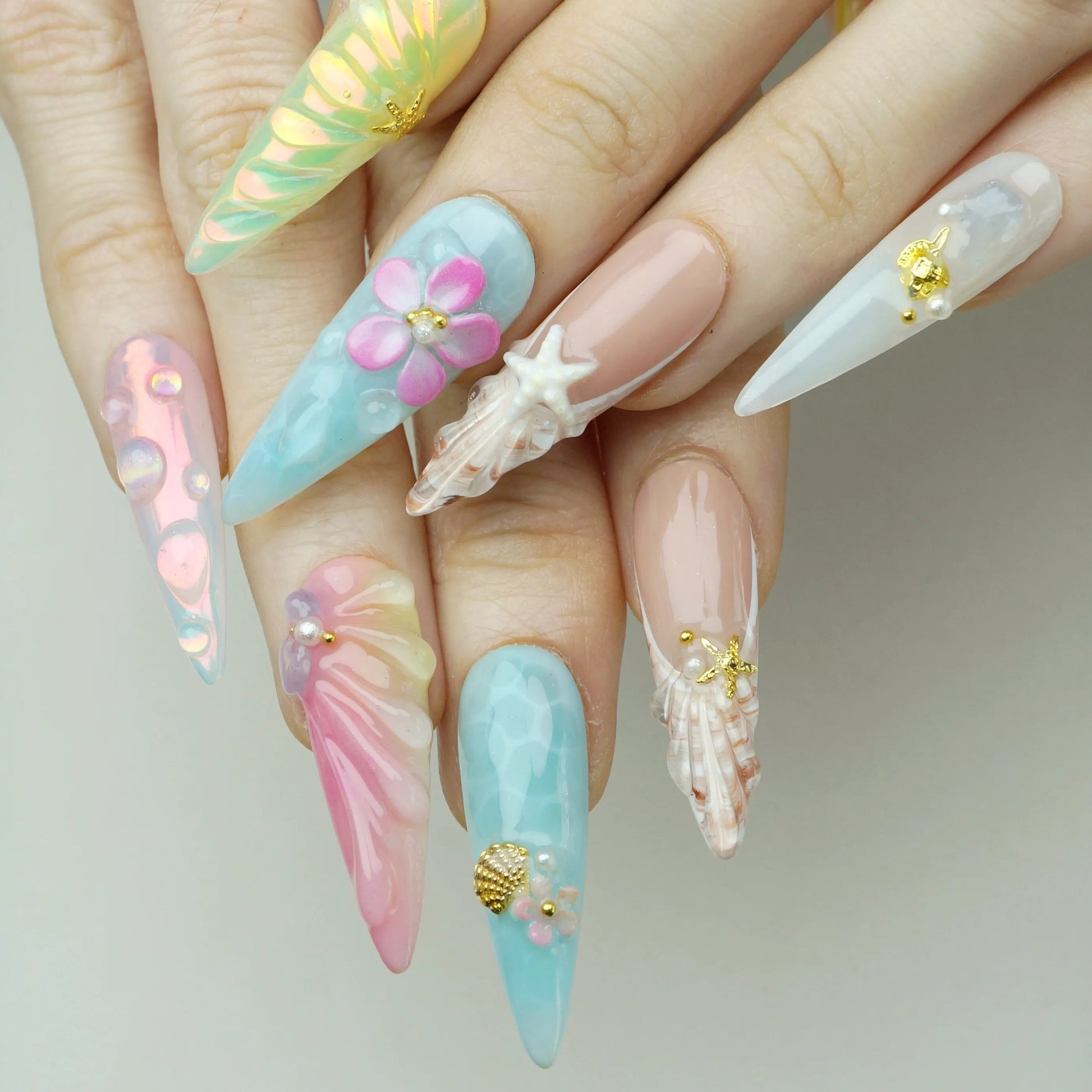Tropical Bliss press-on nails worn on hand model pastel stiletto nails in aqua pink nude and aurora with 3D tropical flower shell starfish and gold scallop charm accents