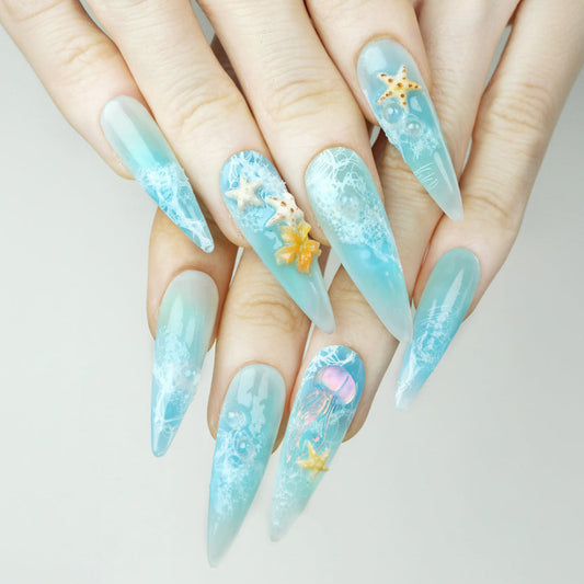 Ocean Bloom press-on nails worn on hand model light blue aqua stiletto nails with 3D jellyfish starfish and orange flower charms sea foam texture summer beach nail art