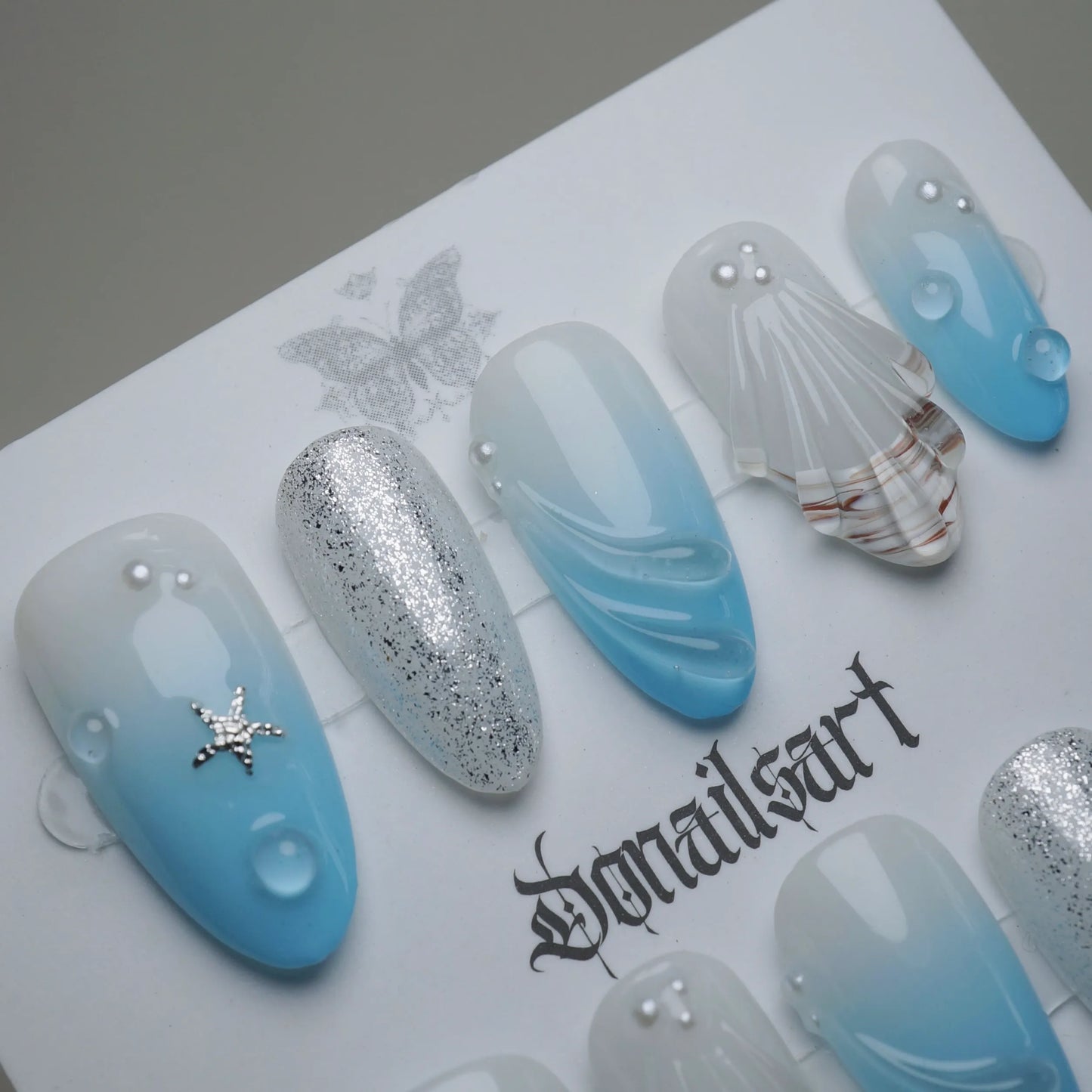 A30 | Blue Lagoon close-up detail showing sculpted shell texture and water droplet accents on a soft blue translucent nail – Donailsart