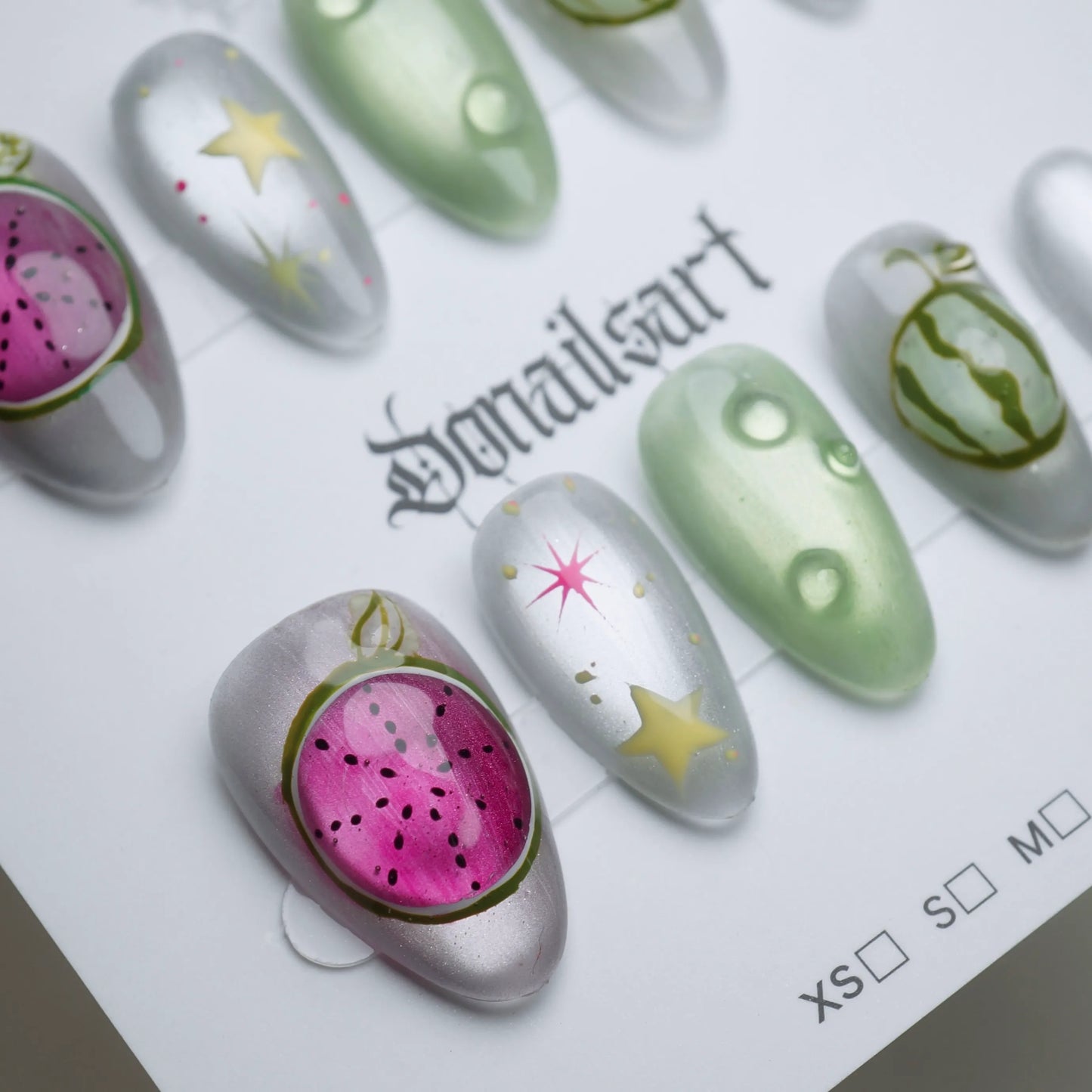 A26 | Melon Mirage close-up detail showing surreal fruit illustration and star accents on chrome silver reflective nails – Donailsart