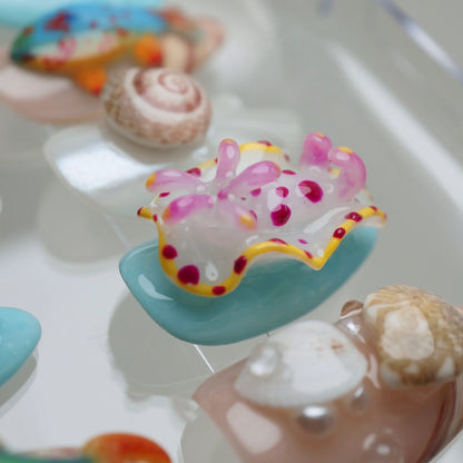 Colorful sea slug toy on a white surface with shells in the background