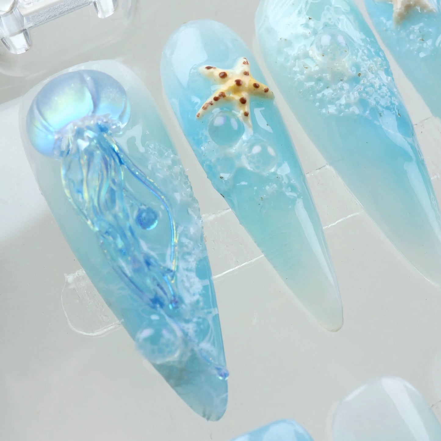 Ocean-inspired summer nails featuring jellyfish art, shell textures, and starfish on soft ombré blue bases