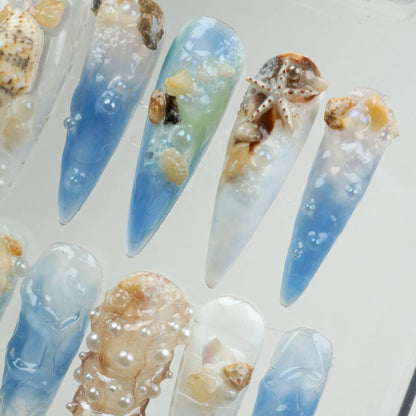 Ocean-inspired nail designs with seashells and blue gradient.