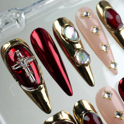 Bold press-on nails from Donailsart with reflective red polish, gold 3D details, and pearl-like stones