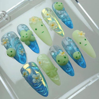 Playful smiski nails featuring mini green character heads, ocean wave textures, and white floral accents