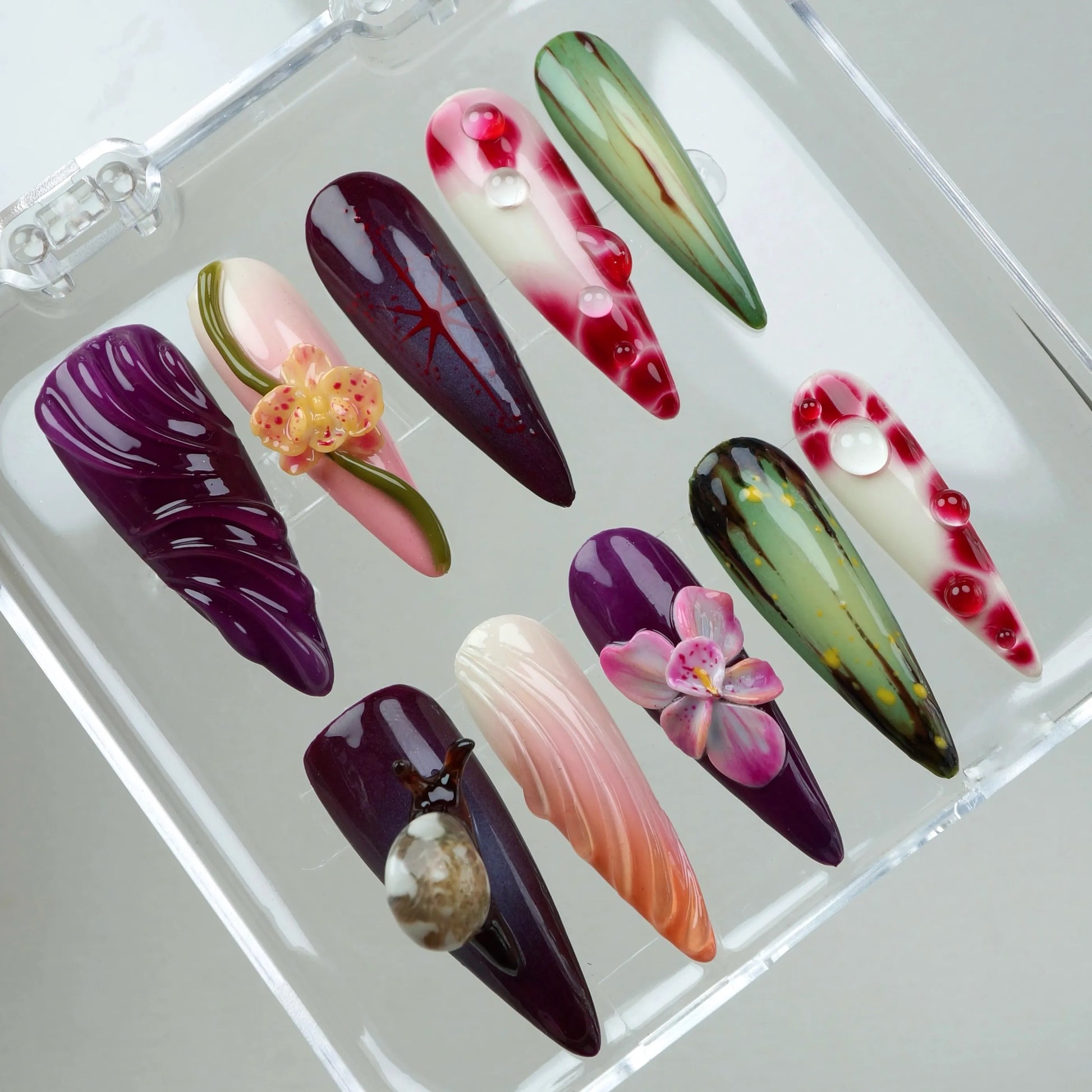 Botanical-inspired flower design nails in rich berry and jungle green colors, decorated with flowers, snails, and water droplets