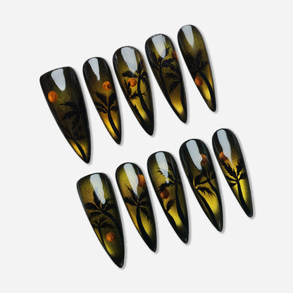 Island Sunrise press-on nail set by Donailsart – cat-eye effect nails with molten gold shimmer, black palm tree silhouettes, and warm tropical sunrise tones