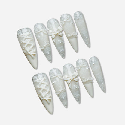 Ivory Keepsake press-on nail set by Donailsart – milky ivory nails with delicate lace patterns, glassy finish, sculpted bows, and tiny pearl accents