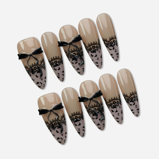 Noir Étreinte press-on nail set by Donailsart – glossy nude base nails with delicate black lace overlays, sculpted satin bow accents, and leopard print tips