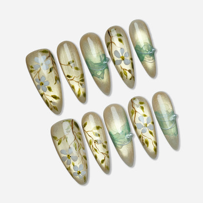 Orchard Veil press-on nail set by Donailsart – luminous golden base nails with delicate white florals on fine vine details and translucent mint ribbon accents
