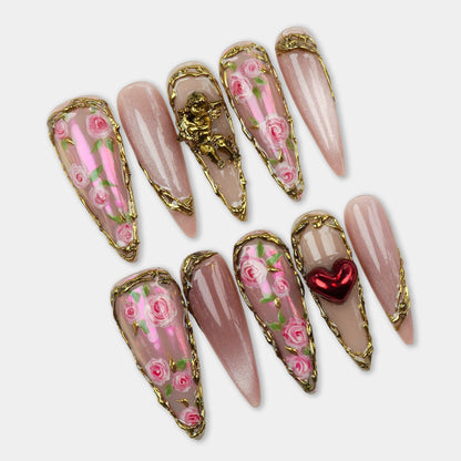Elegant press-on nails with hand-painted pink roses, gold metal borders, and 3D details like a heart and cherub.