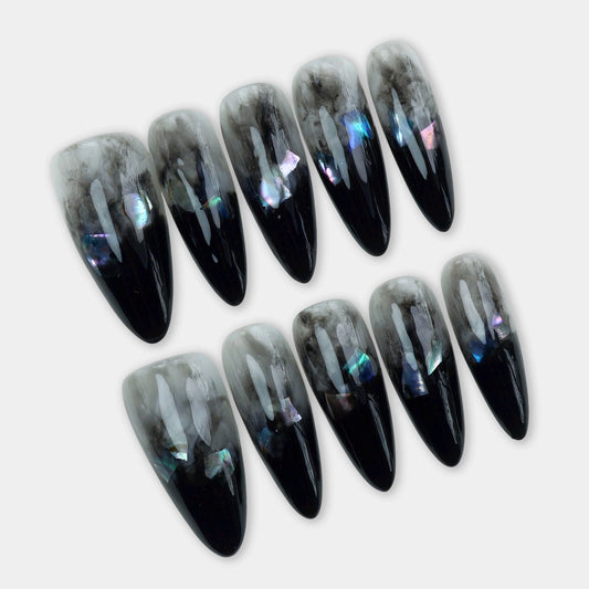 Long almond-shaped press-on nails with a black-to-clear ombré base, smoky marble effect, and subtle holographic flakes.