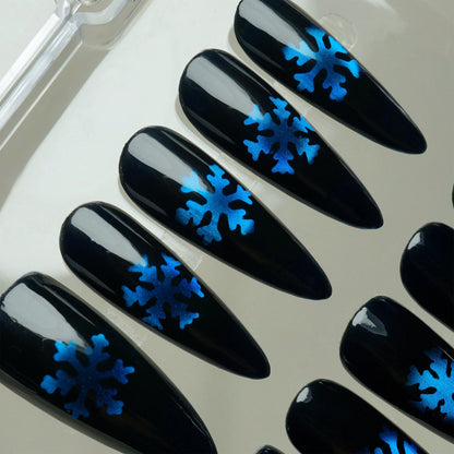 Glossy black press-on nails with metallic blue snowflake designs, inspired by a frosty winter night.
