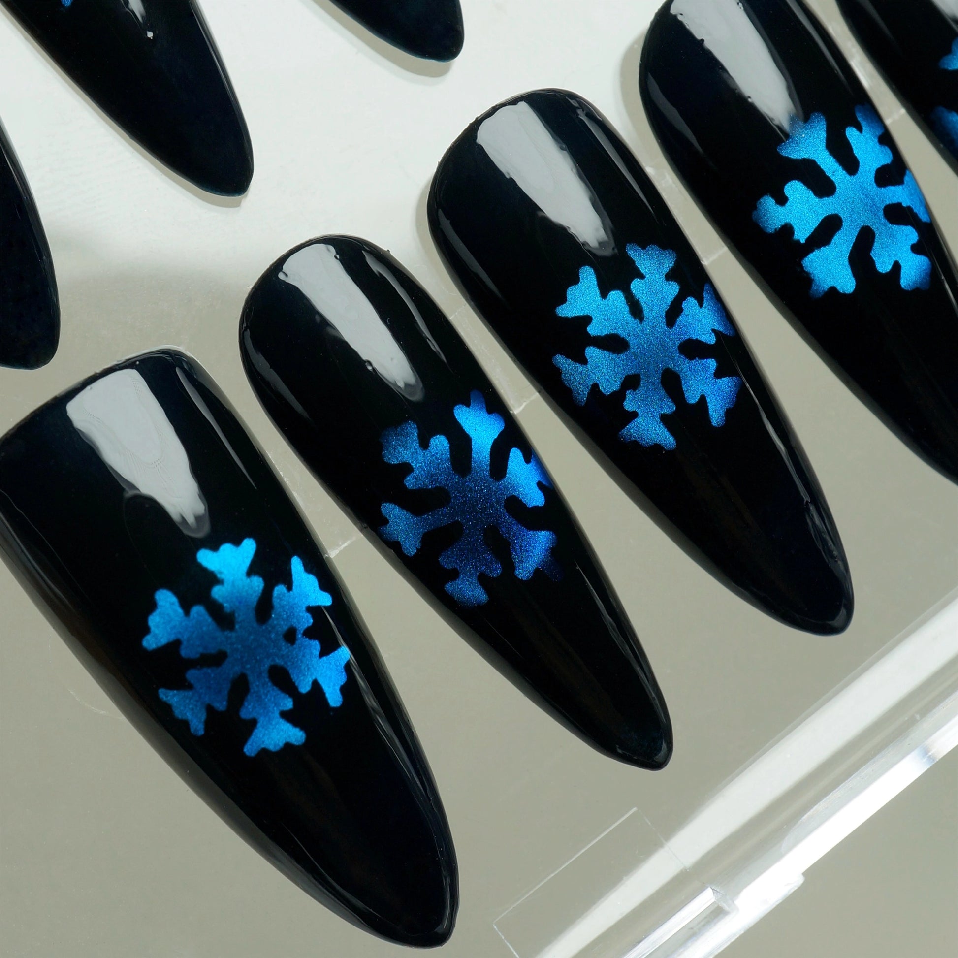 Black nails with blue snowflake designs on a light gray background