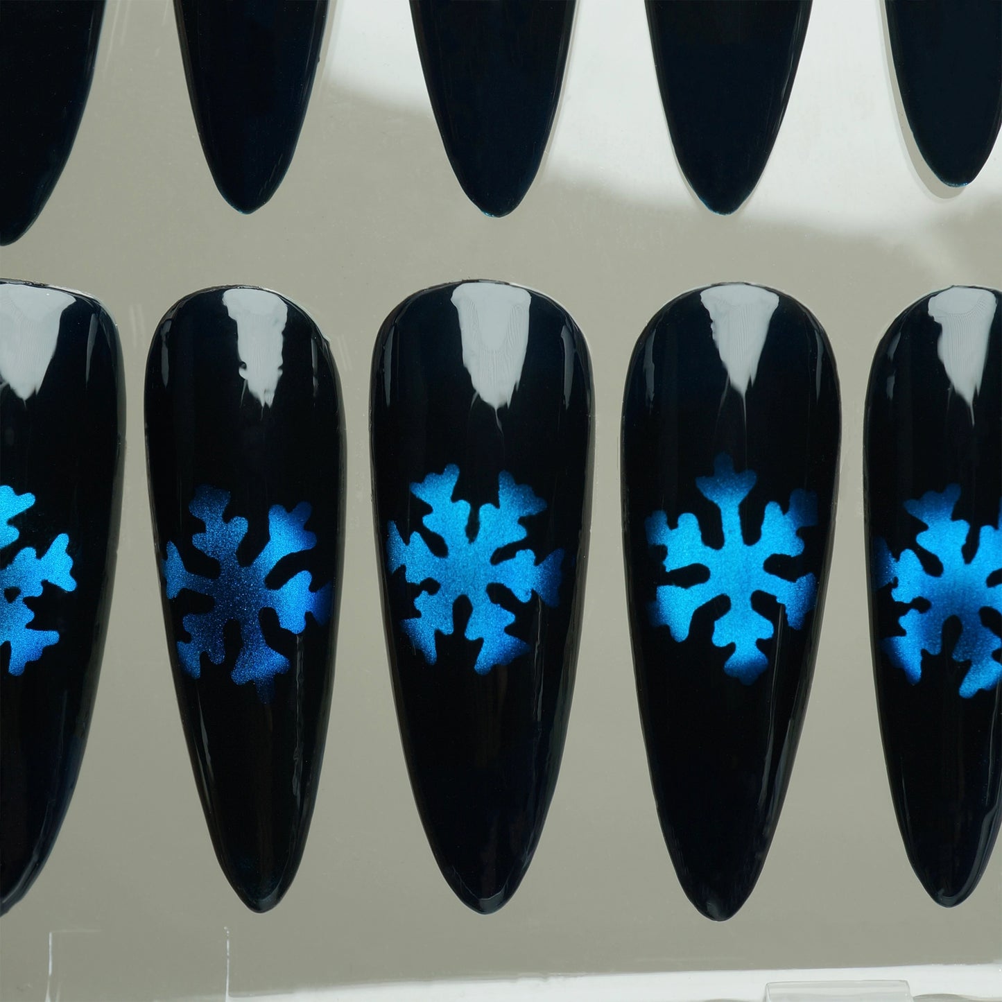 Black nail extensions with blue snowflake designs on a clear background